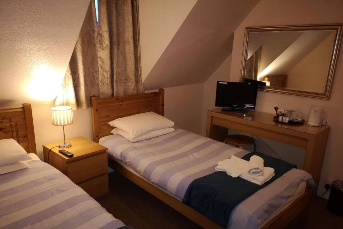 A bedroom with two beds, a desk, a television, and a mirror.
