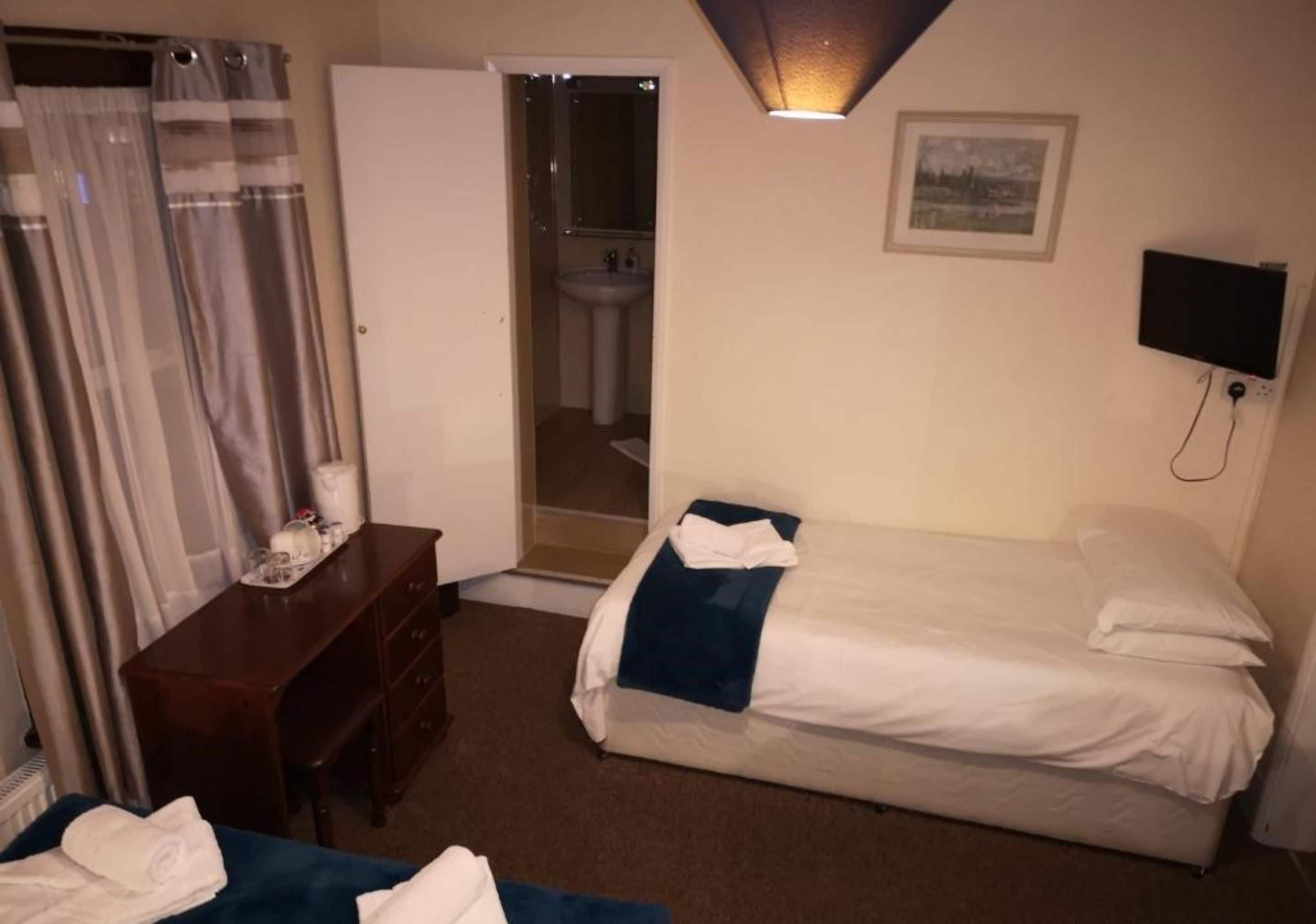 A hotel room with a bed, a desk, a chair, a bathroom visible through an open door, and a mounted TV.