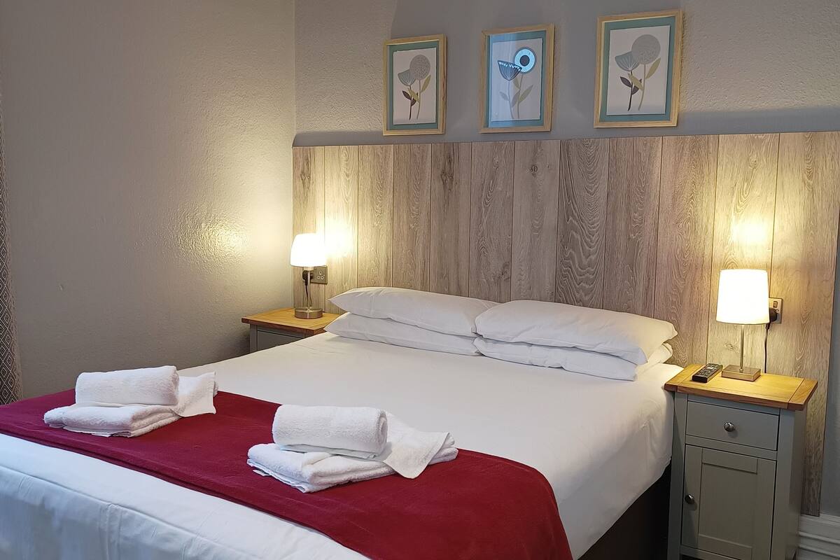 A neatly made bed with white linens and a red blanket, two bedside lamps, and a wooden headboard.