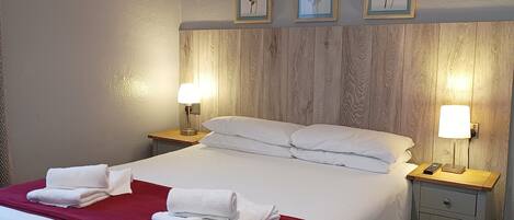 Cama bem arrumada com lençóis brancos e um cobertor vermelho, duas luminárias de cabeceira e uma cabeceira de madeira.