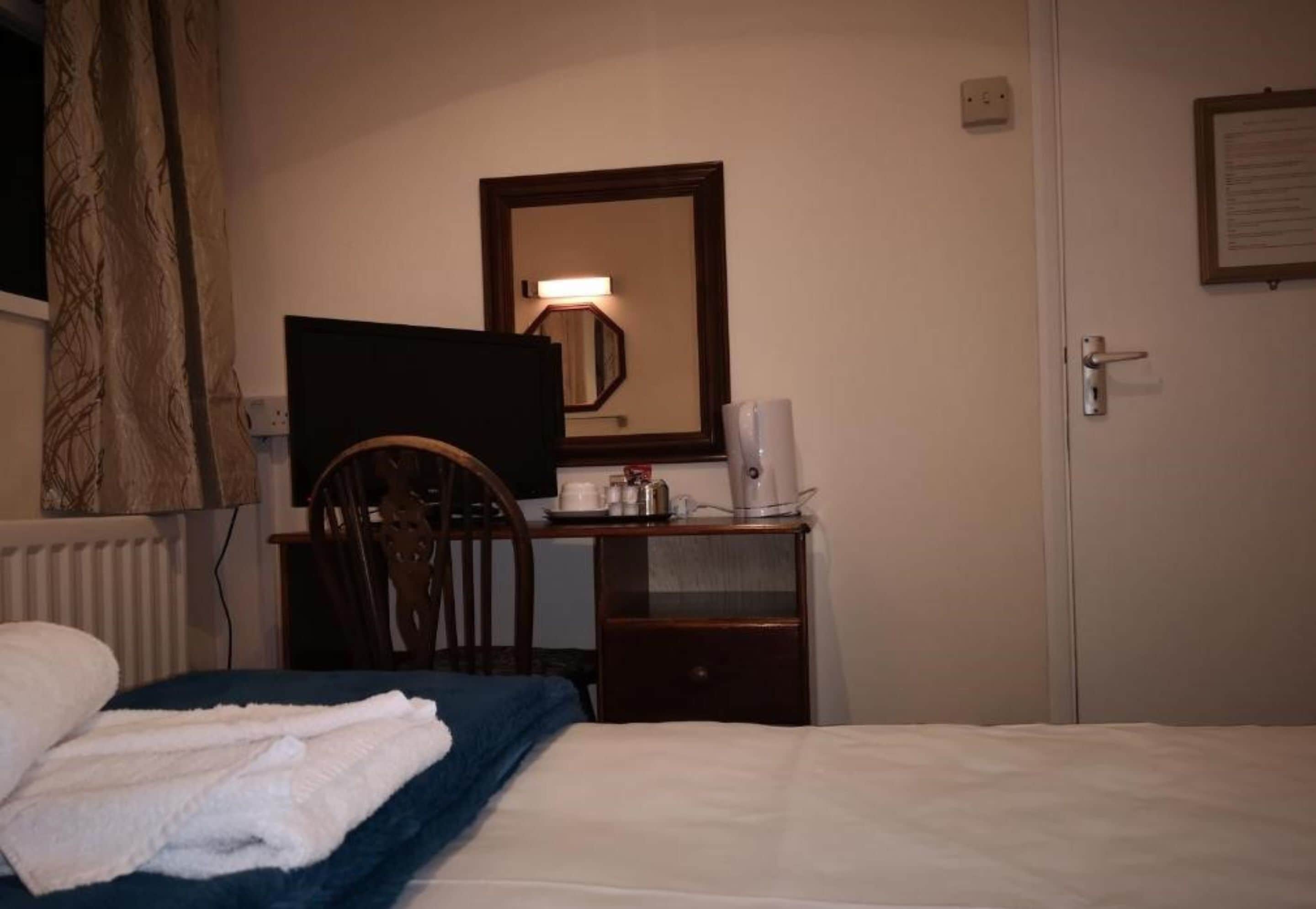 A hotel room with a bed, a desk with a computer, a chair, and a door.