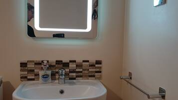 A bathroom with a white sink, a mirror with a light, and a towel rack.