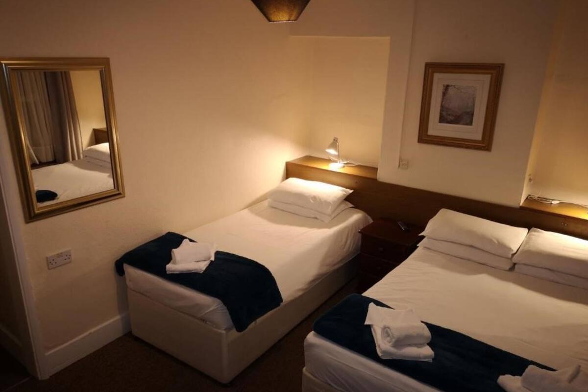 A hotel room with two single beds, a bedside table with a lamp, a mirror, and a framed picture on the wall.