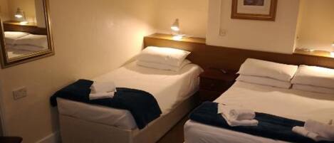 Ein Hotelzimmer mit zwei Betten, einem Nachttisch mit Lampe, einem Spiegel und einem gerahmten Bild an der Wand.