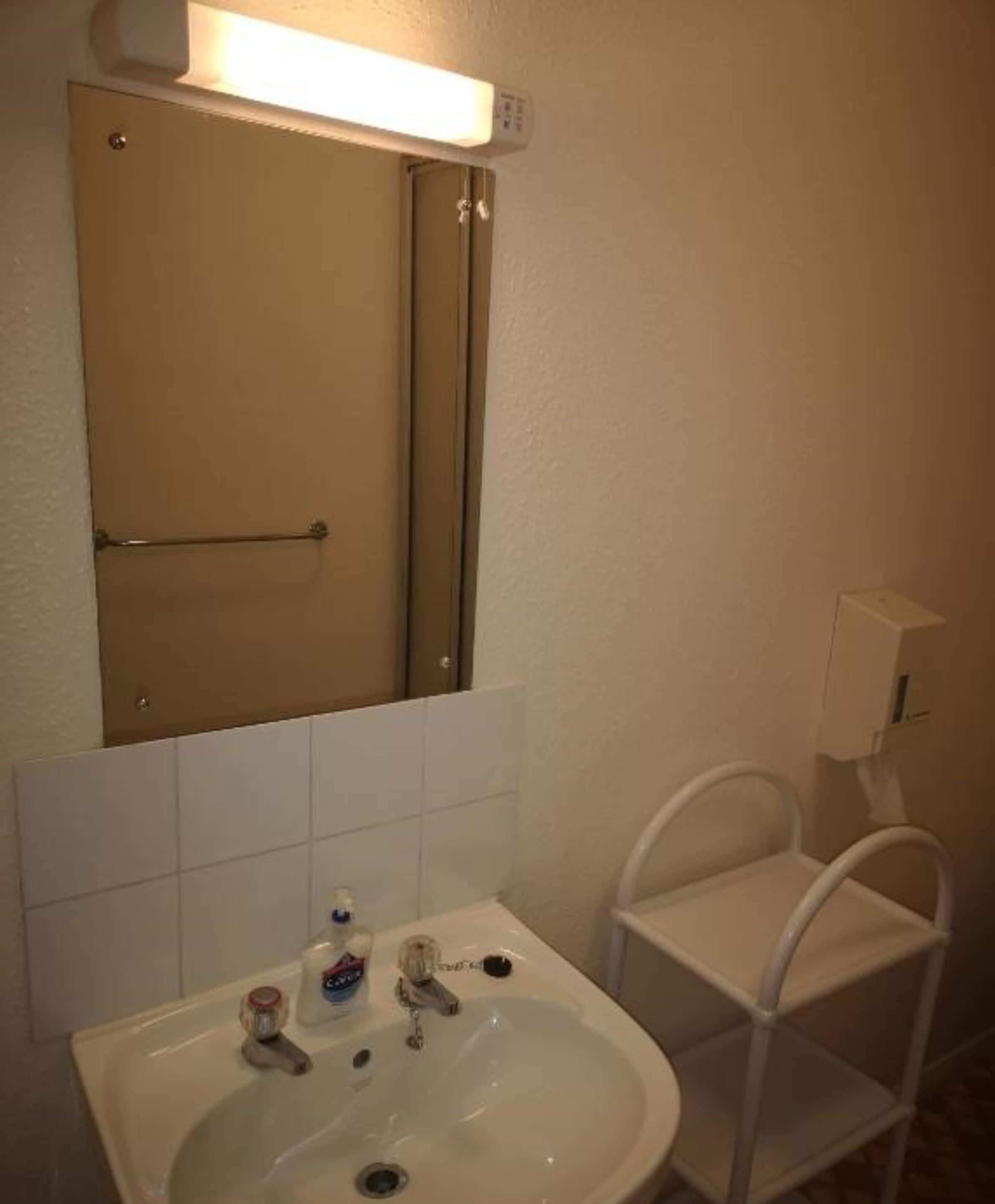 Un baño con lavamanos, espejo, toallero y un pequeño estante.