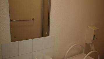 Un baño con lavamanos, espejo, toallero y un pequeño estante.