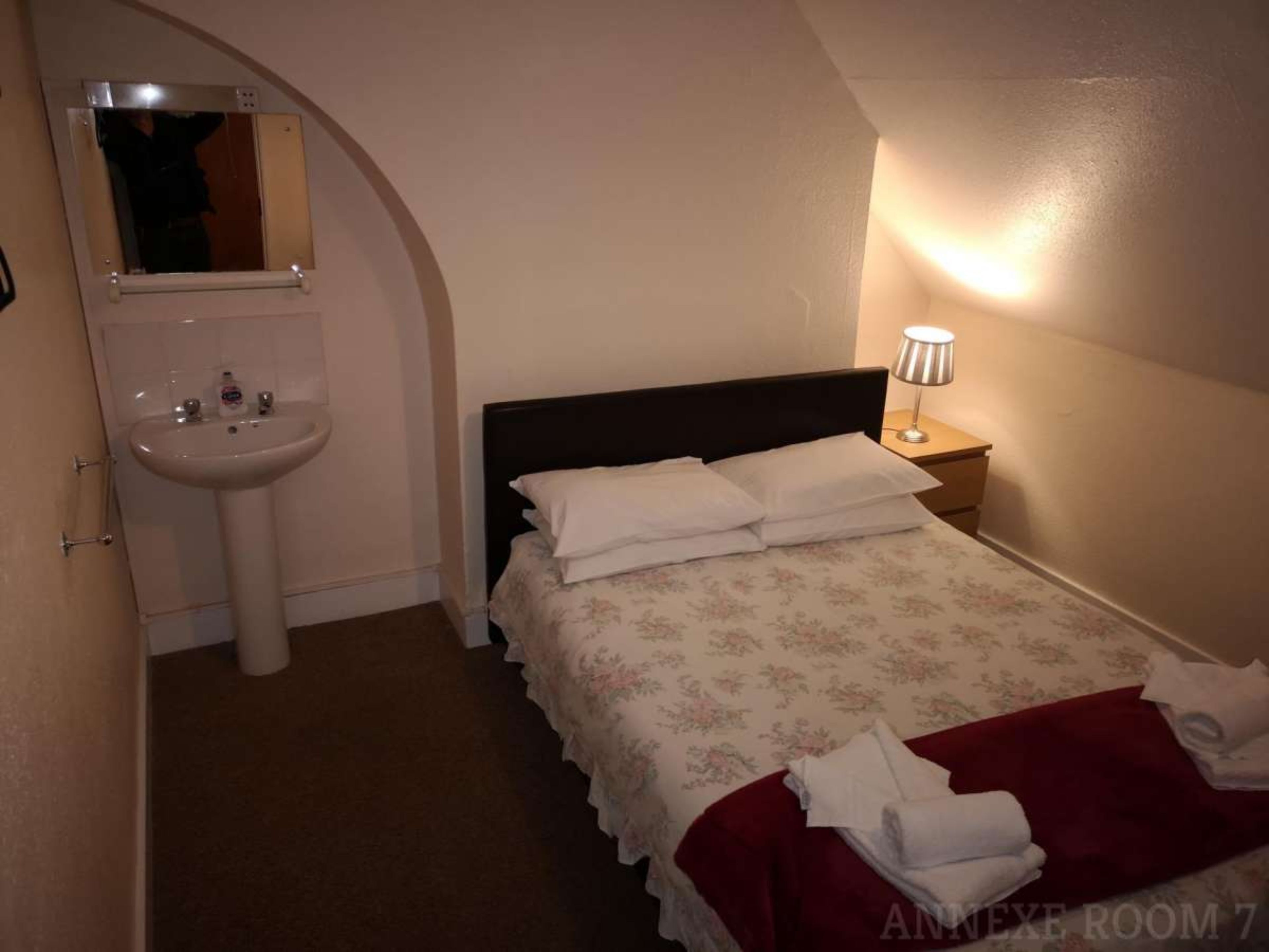 Un dormitorio con cama, mesita de noche, lámpara, lavamanos y espejo.