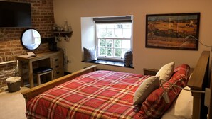A bedroom with a bed, a dresser, a mirror, a window with a view, and a painting on the wall. - The White Hart (Newport Pagnell)