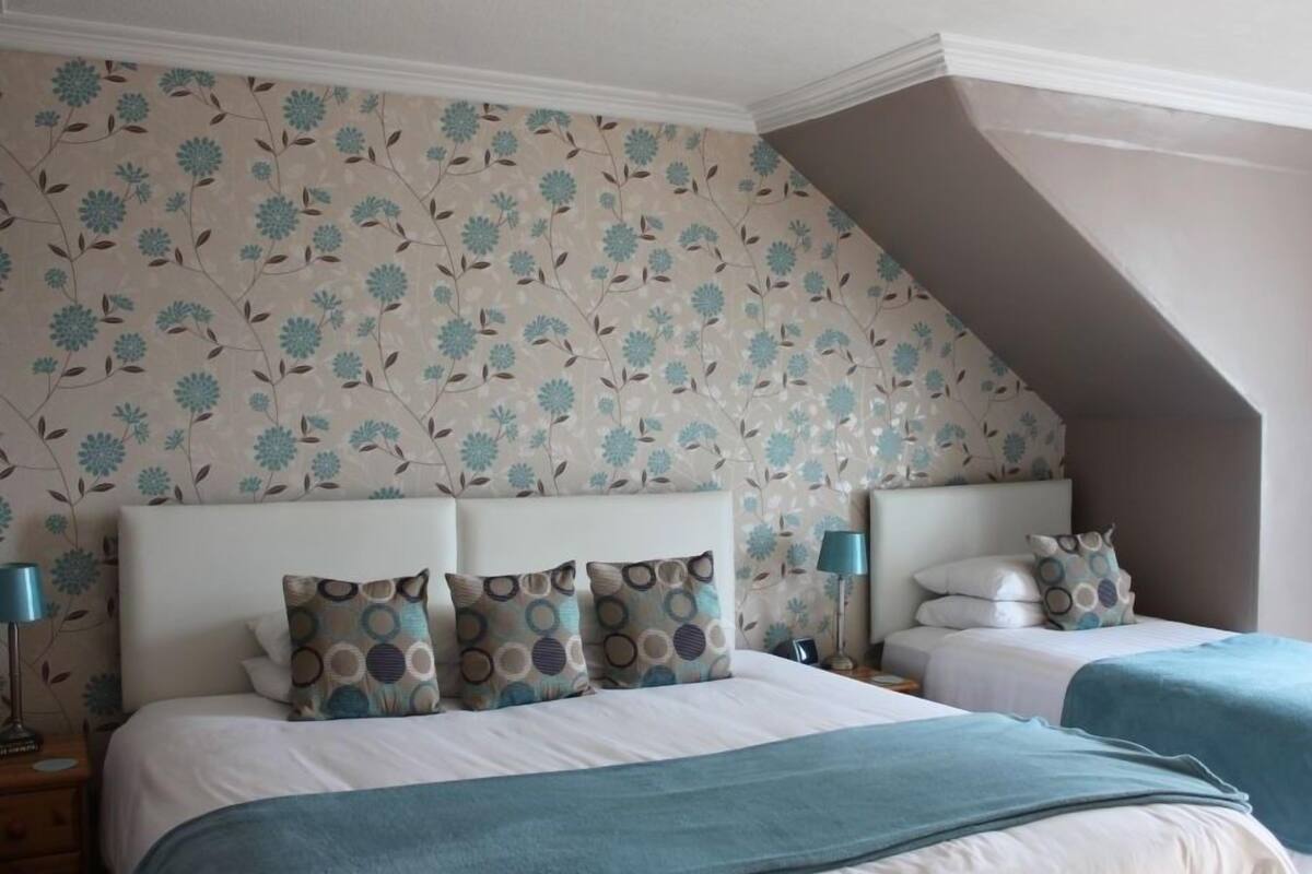 A bedroom with two beds, floral wallpaper, and a sloped ceiling.