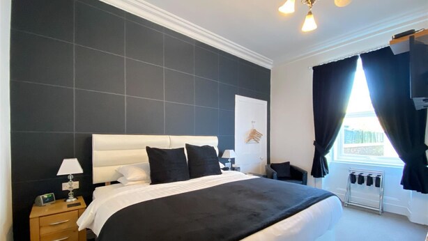 A modern hotel room with a large bed, bedside tables, a nightstand, a lamp, a radiator, and a window with curtains. - Rosebank Guest House (Perth)