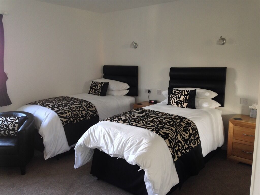 Une chambre d’hôtel avec deux lits, chacun agrémenté de draps à motifs noir et blanc, une table de chevet en bois et un fauteuil en cuir noir.
