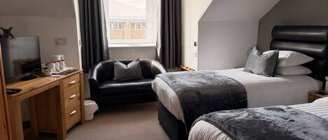 A bedroom with a desk, two beds, a window with curtains, and a view of the outside.