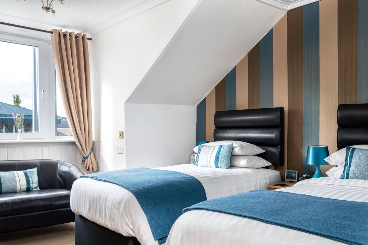 A hotel room with two beds, a sofa, a window with curtains, and a striped wall.