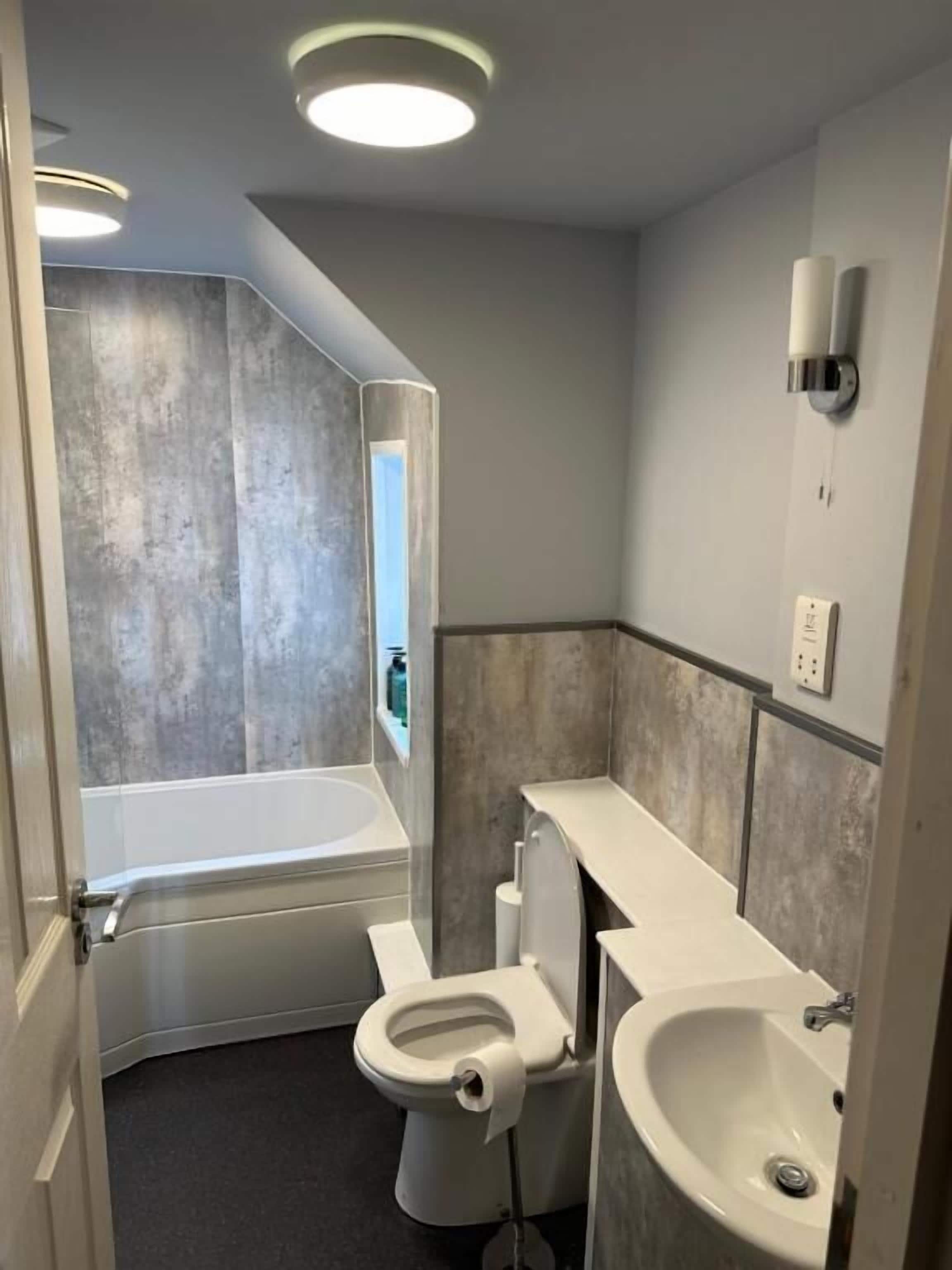 A bathroom with a bathtub, toilet, and sink, with a mirror and light fixtures.