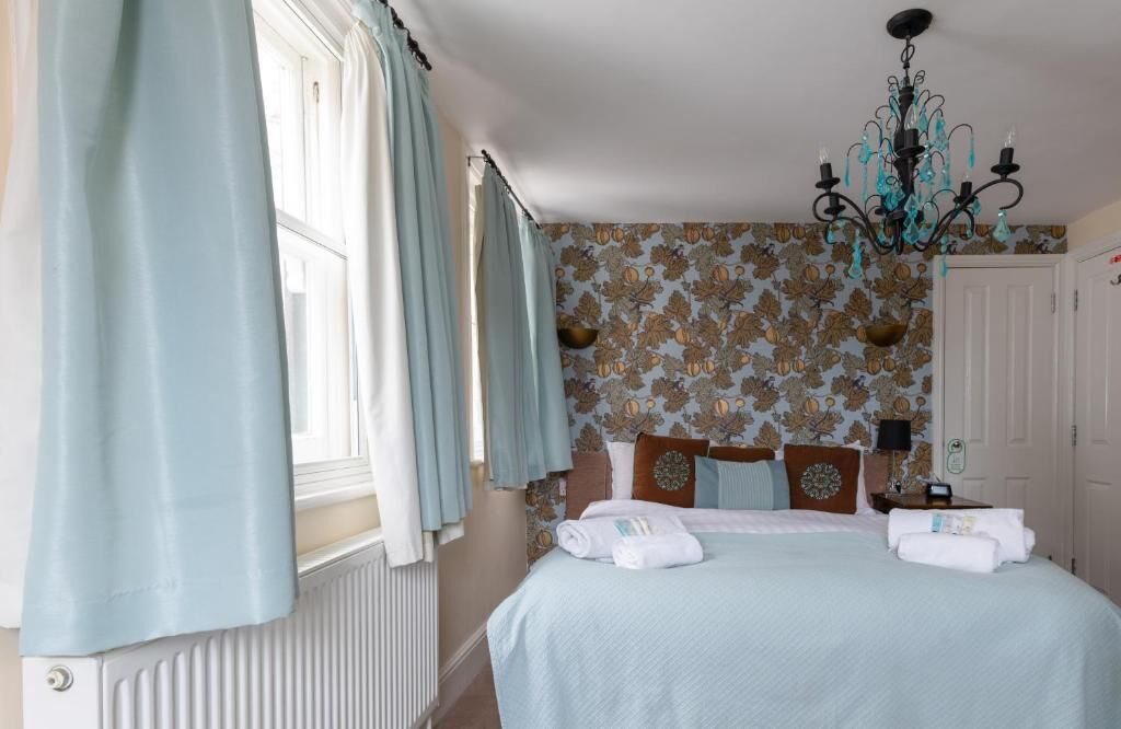 A bedroom with a bed, curtains, a chandelier, and patterned wallpaper.