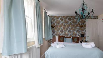 A bedroom with a bed, curtains, a chandelier, and patterned wallpaper.