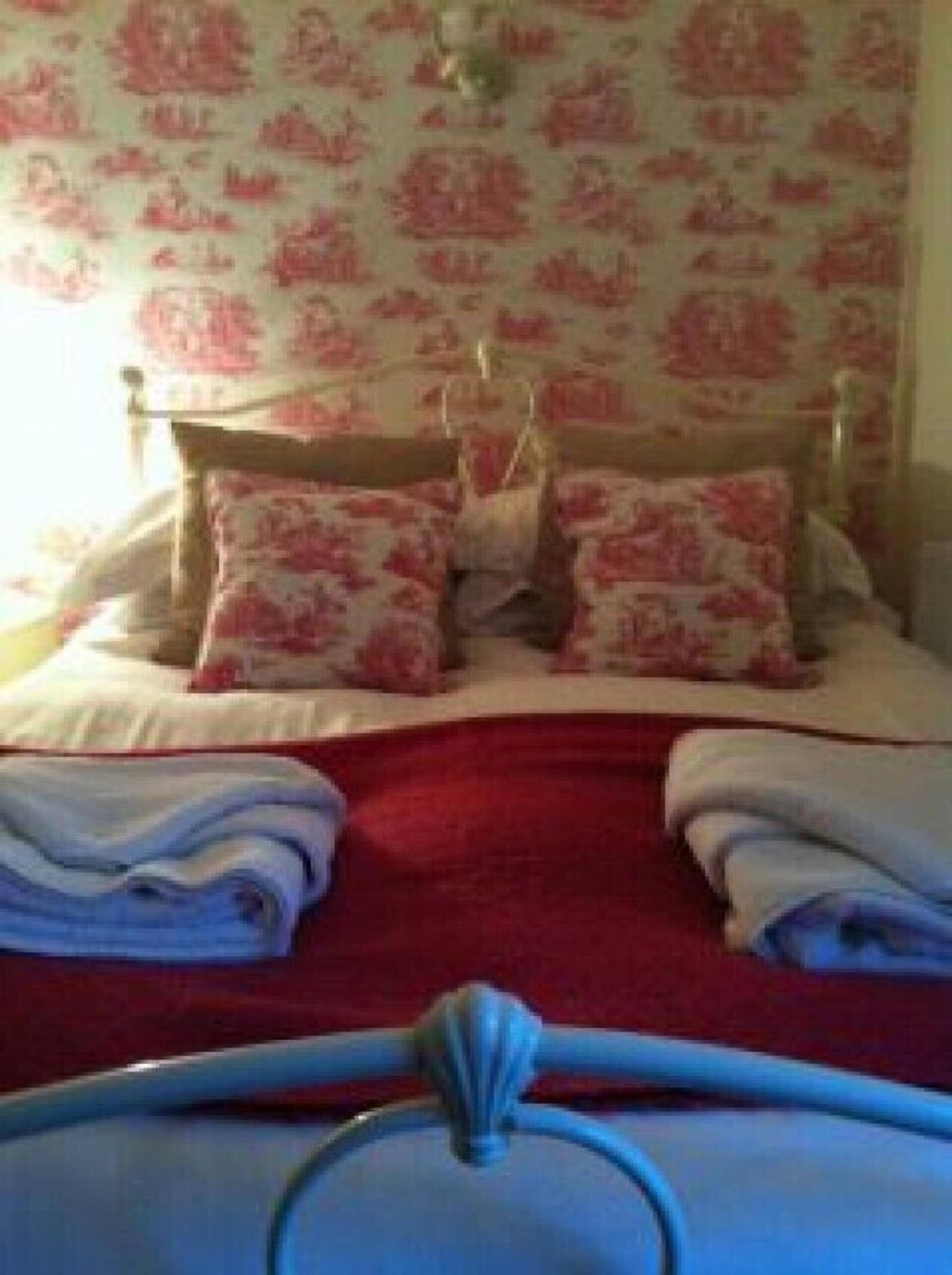 Un lit bien fait, avec une couverture rouge, deux oreillers et des serviettes pliées.