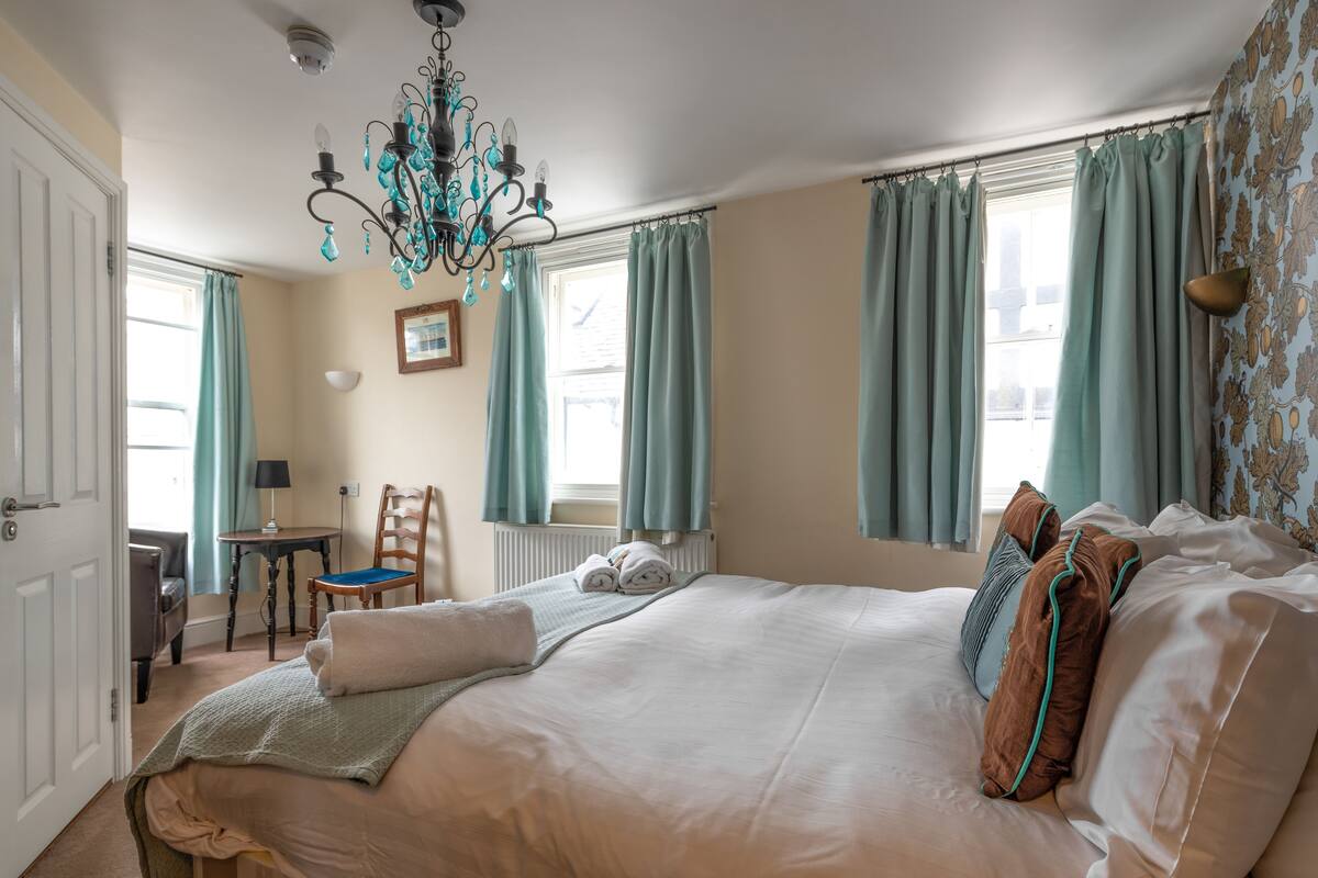 A bedroom with a large bed, a chair, a table, and a chandelier.