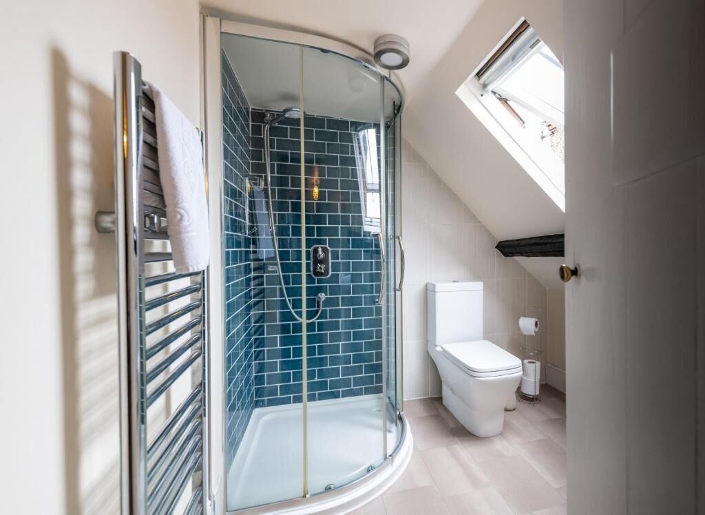 A modern bathroom with a glass-enclosed shower, a white toilet, and a skylight.