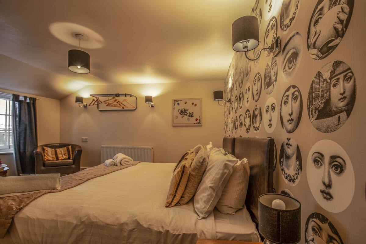 A bedroom with a large bed, a chair, and a wall decorated with various circular portraits.
