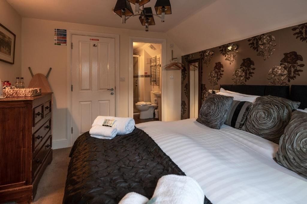 A bedroom with a bed, a dresser, a shower area, and a door leading to a bathroom.