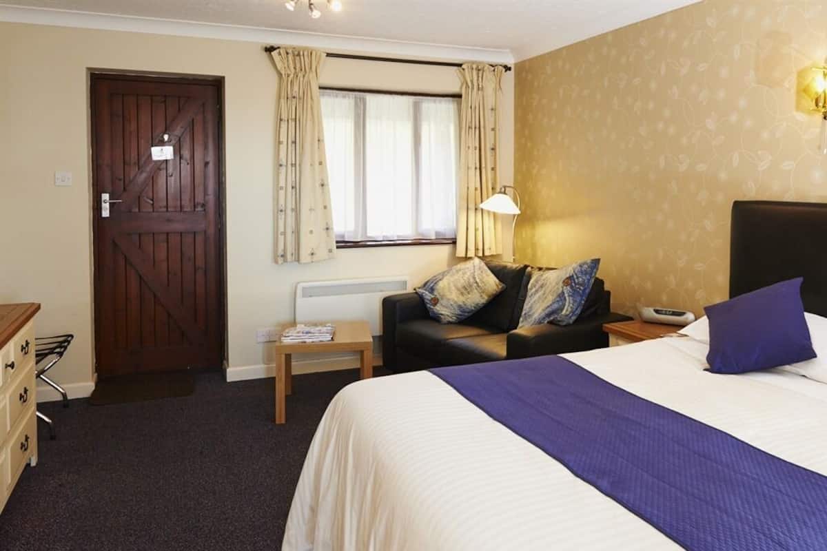 Una habitación de hotel con cama, mesita de noche, lámpara, cómoda y puerta.