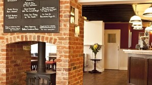 A cozy room with a brick fireplace, a wooden floor, and a dining area with a table and chairs. - The Marsham Arms Inn (Norwich)