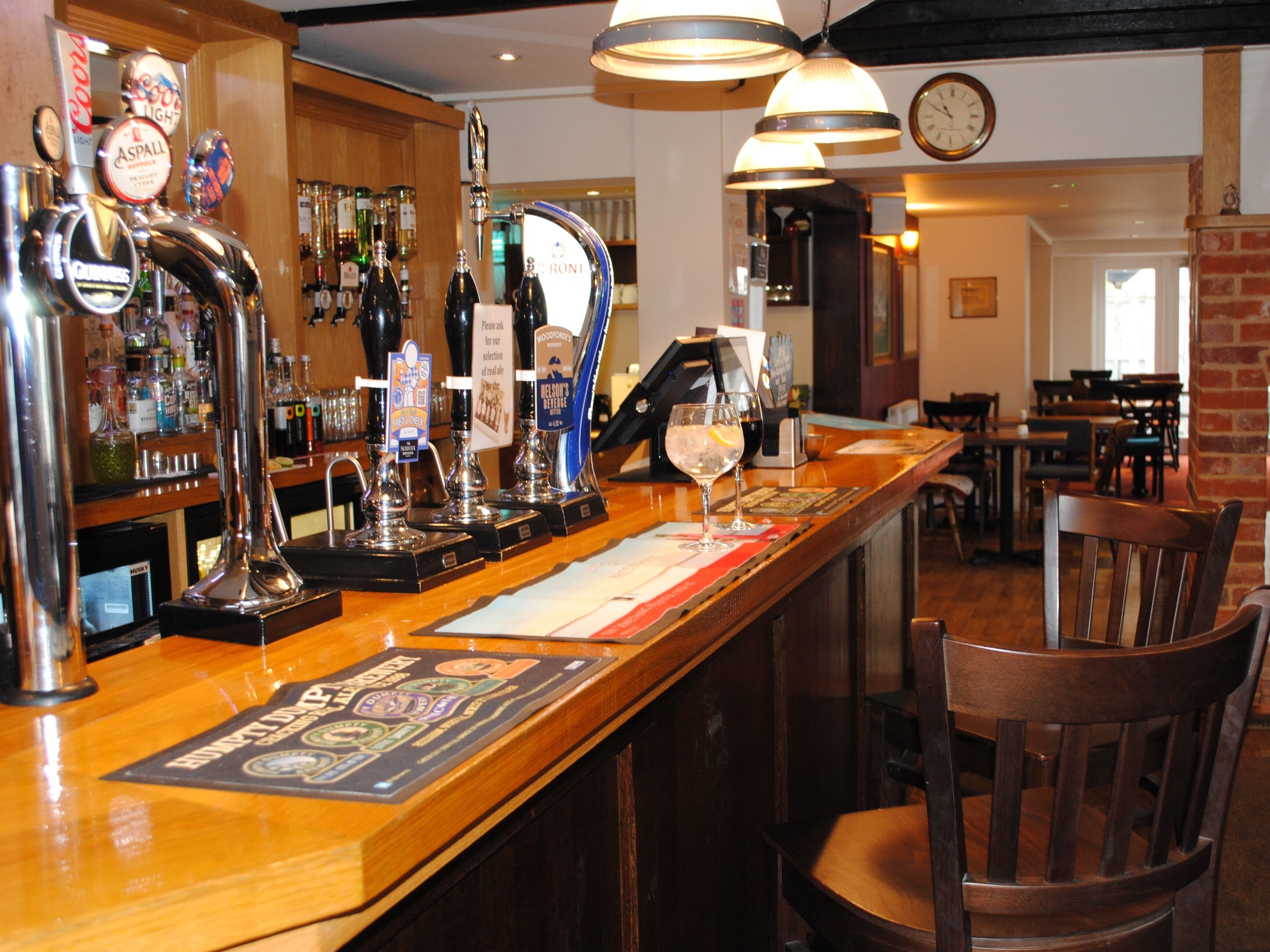 A bar area with multiple beer taps, a clock on the wall, and a menu on the counter.