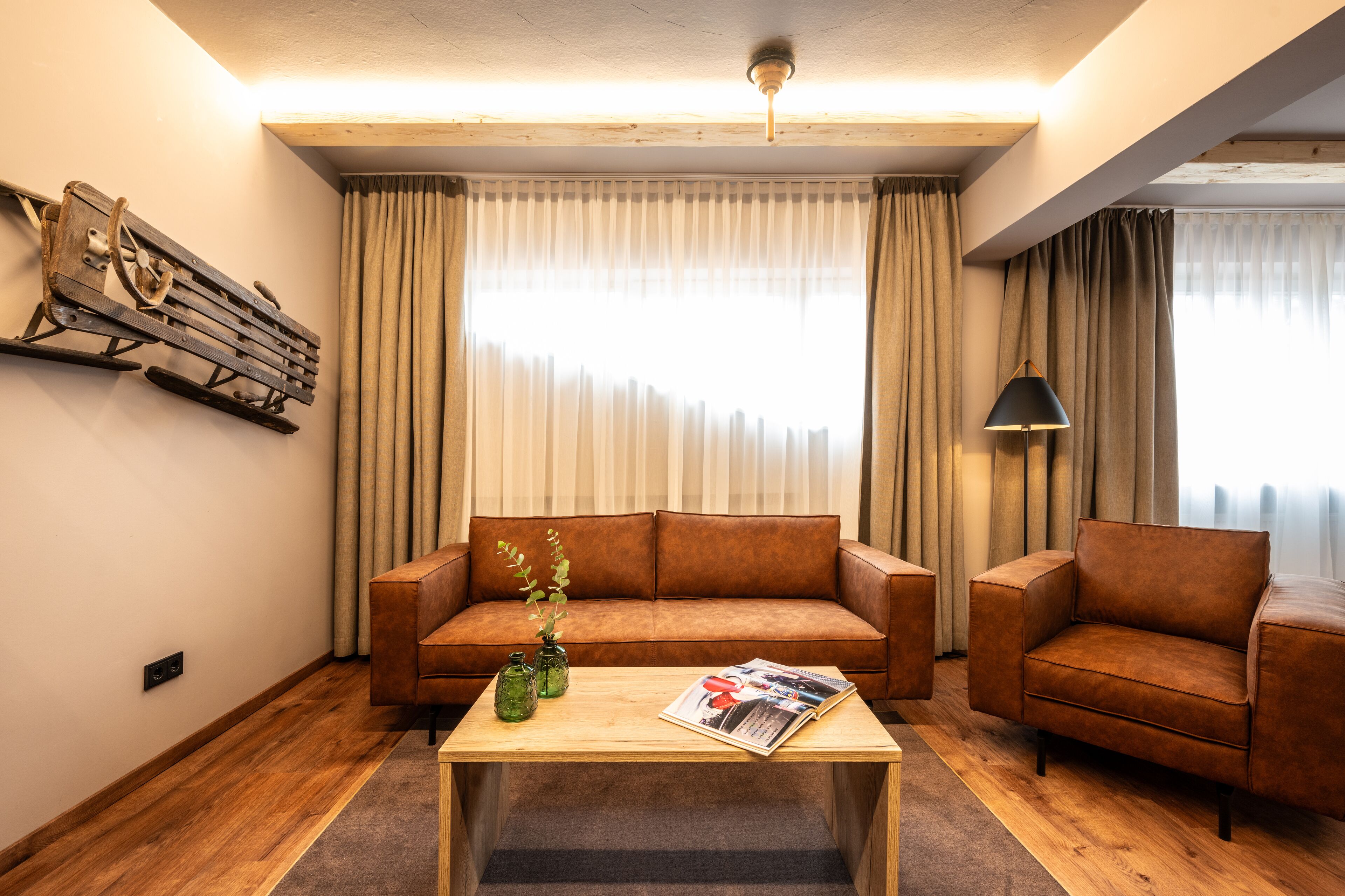 A living room with a wooden floor, a brown leather sofa, a wooden coffee table, and a lamp.