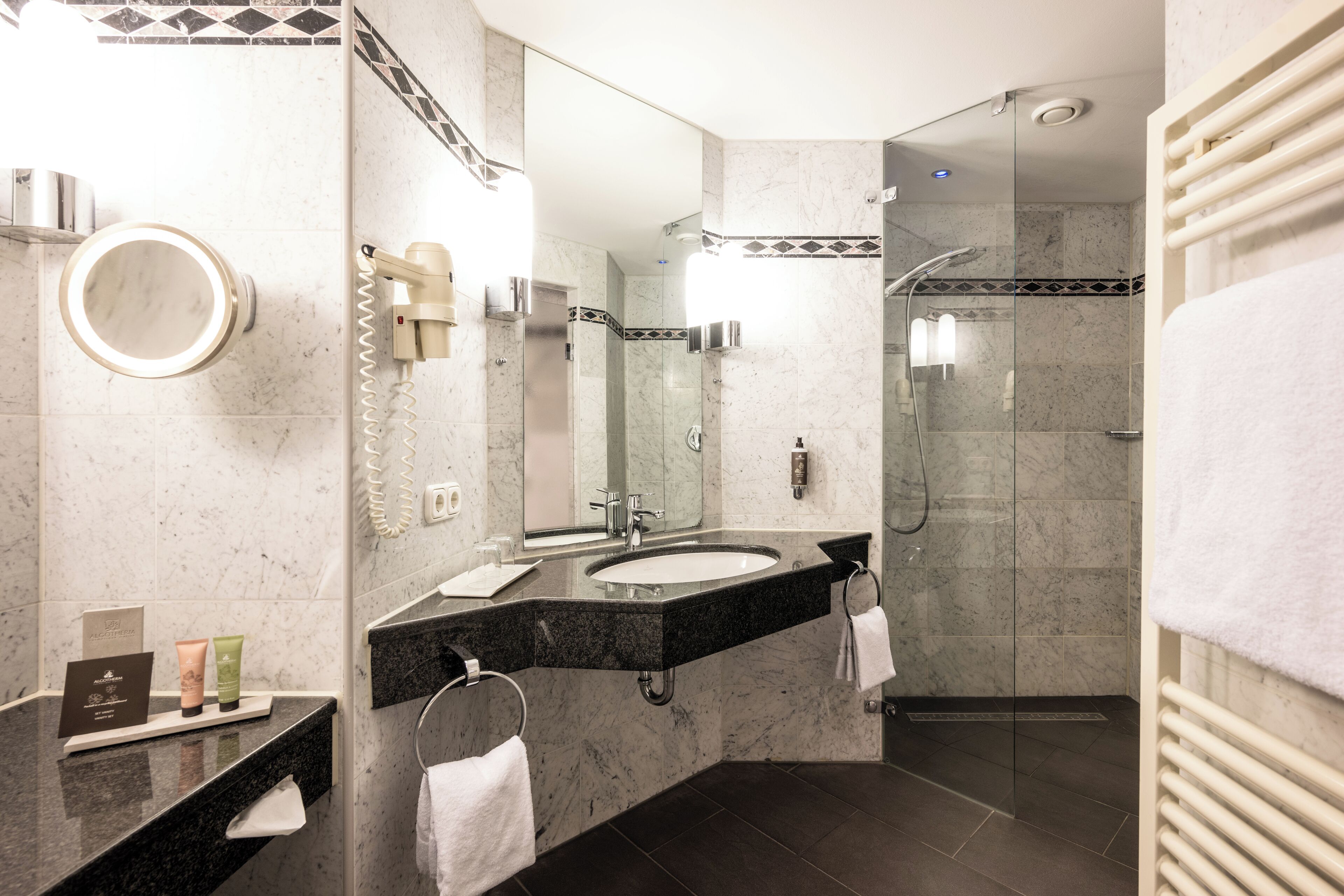A modern bathroom with a dual sink vanity, a large mirror, a glass-enclosed shower, and a towel rack.