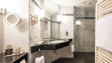 A modern bathroom with a dual sink vanity, a large mirror, a glass-enclosed shower, and a towel rack.