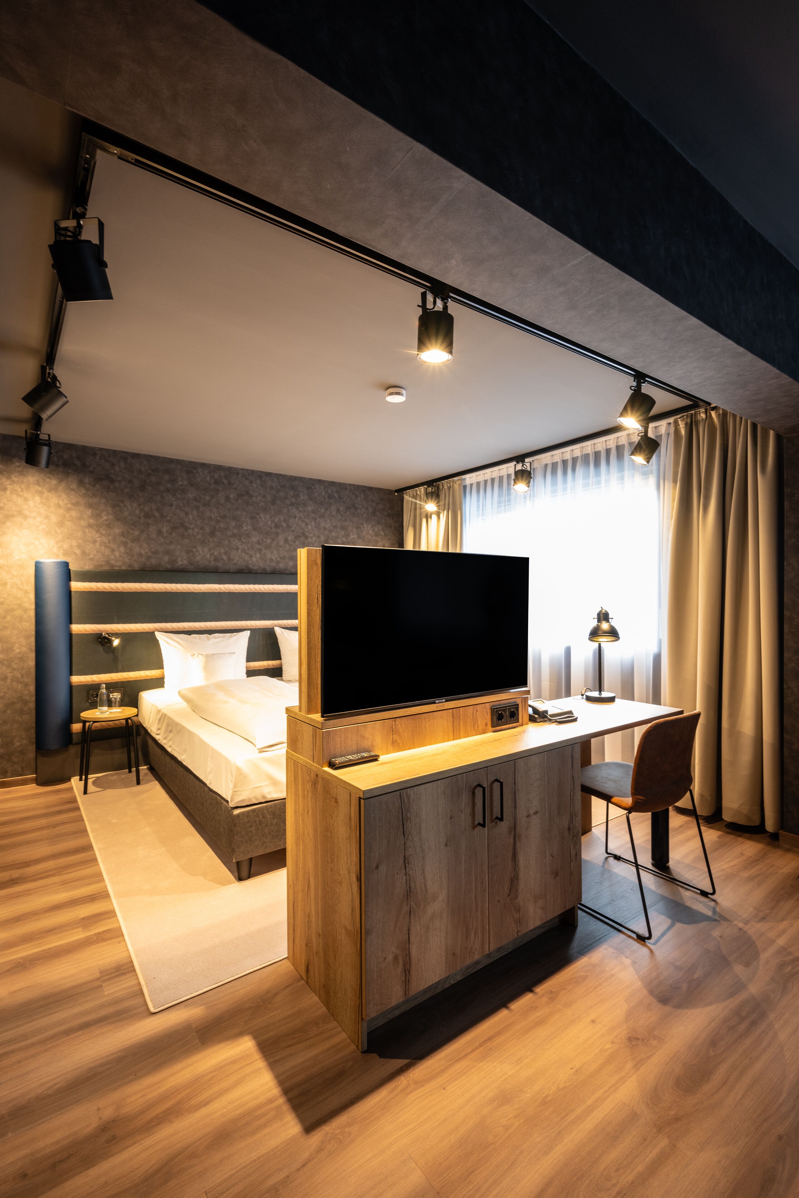 Ein modernes Hotelzimmer mit einem großen Bett, einem Schreibtisch, einem Flachbildfernseher, einem Sessel und einem kleinen Tisch.
