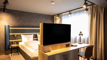 Ein modernes Hotelzimmer mit einem großen Bett, einem Schreibtisch, einem Flachbildfernseher, einem Sessel und einem kleinen Tisch.
