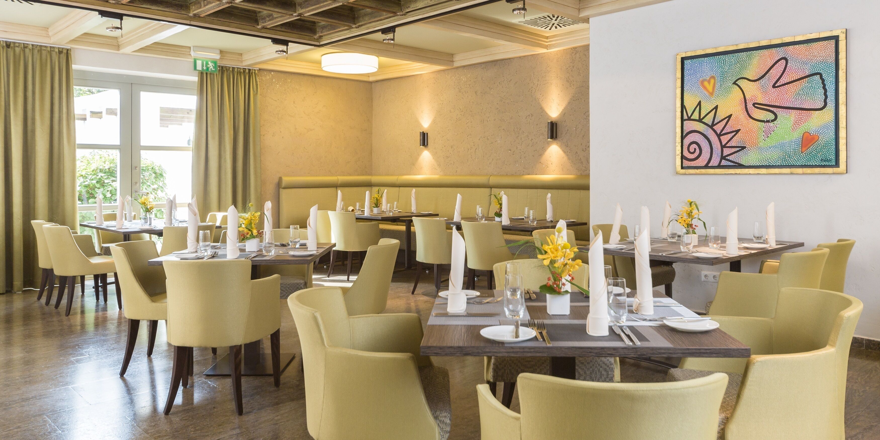A dining area with tables set for service, a bench, and a wall-mounted artwork.