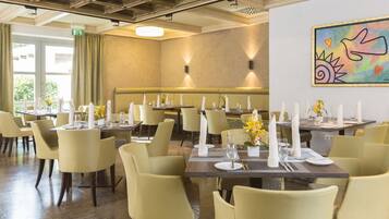A dining area with tables set for service, a bench, and a wall-mounted artwork.