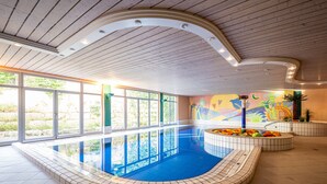 Una piscina interior con suelo de baldosas, techo curvo y amplios ventanales.
