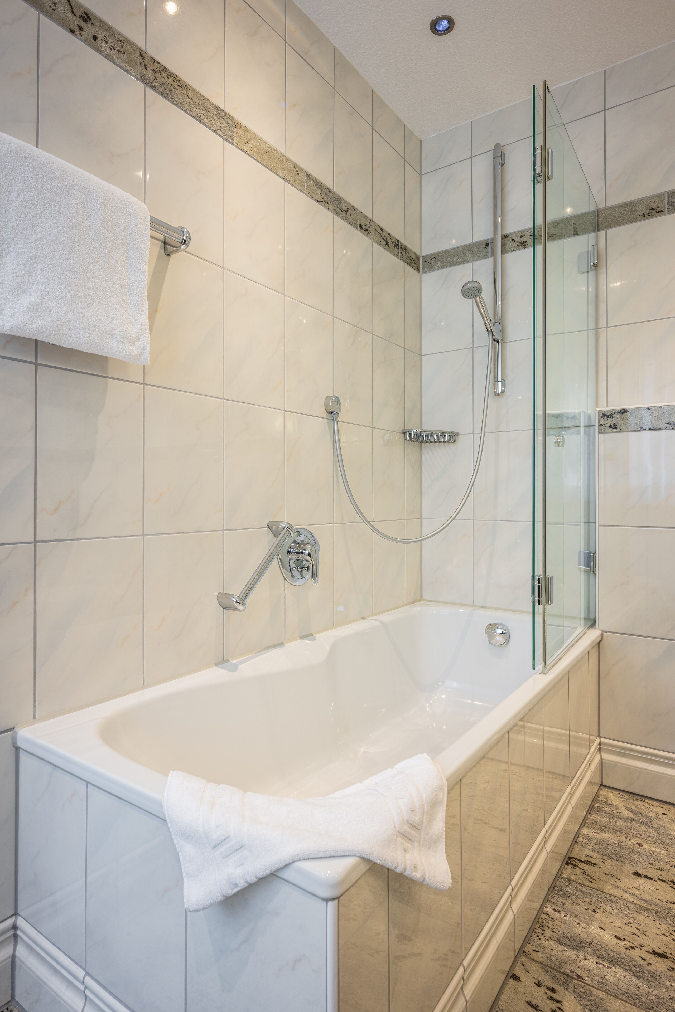 A modern bathroom with a glass-enclosed shower, a standalone bathtub, and a white towel on the tub.