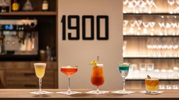 A bar counter with four different cocktails, a shelf with bottles, and a wall with the number 1900.