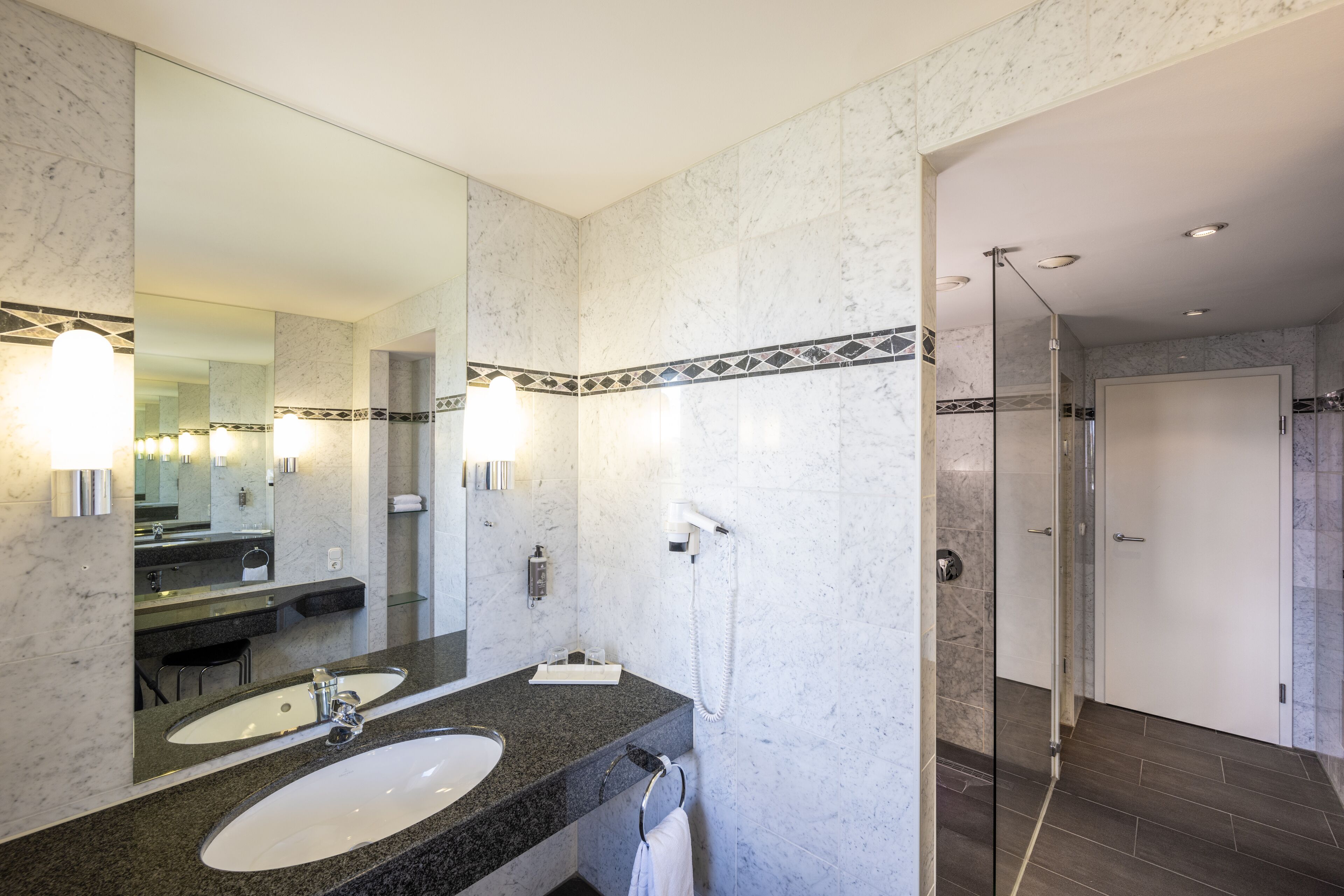 Une salle de bain moderne avec un grand miroir, deux lavabos, un porte-serviettes et une douche à parois de verre.