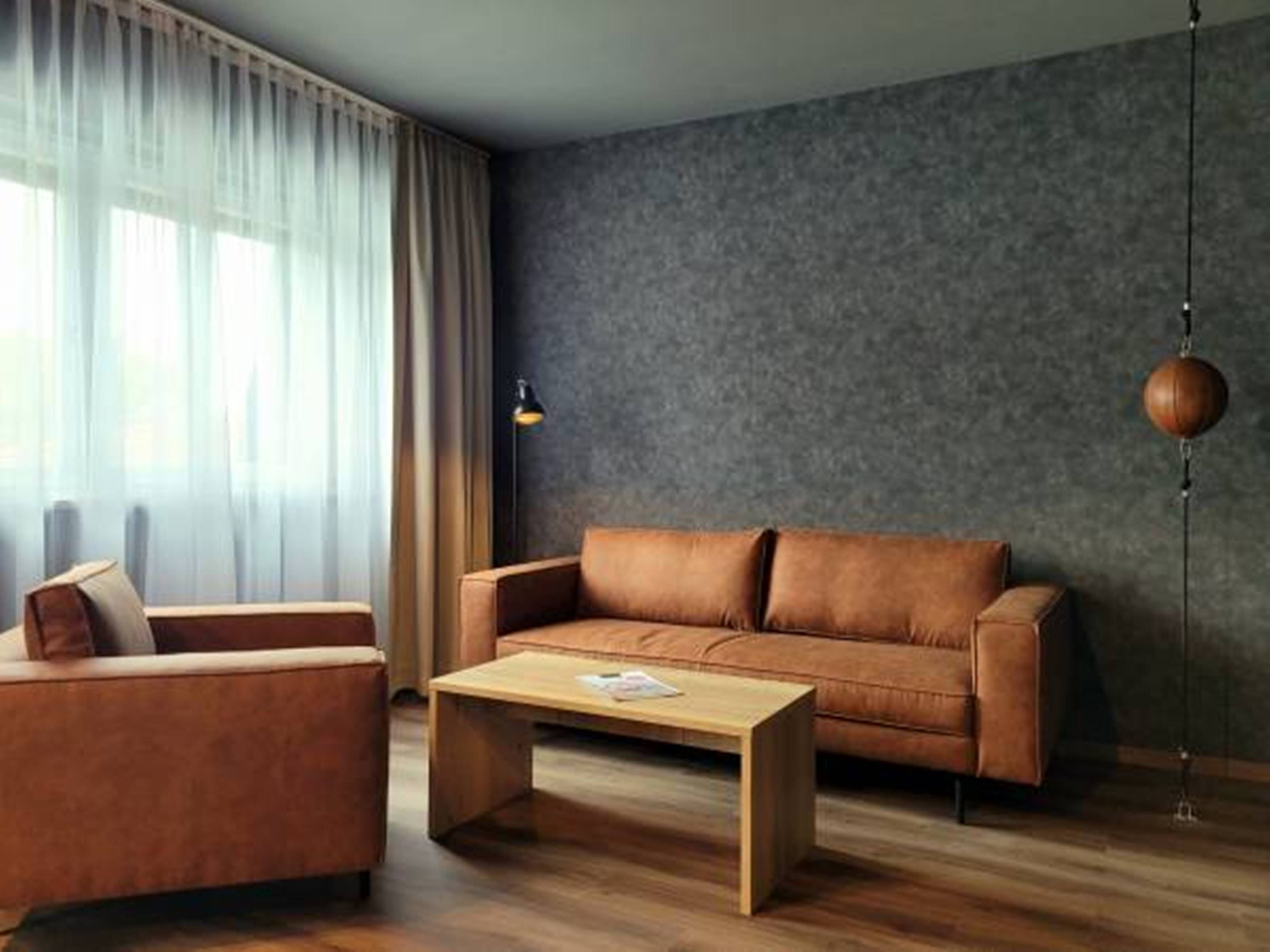 A modern living room with a brown leather sofa, a wooden coffee table, and a lamp.