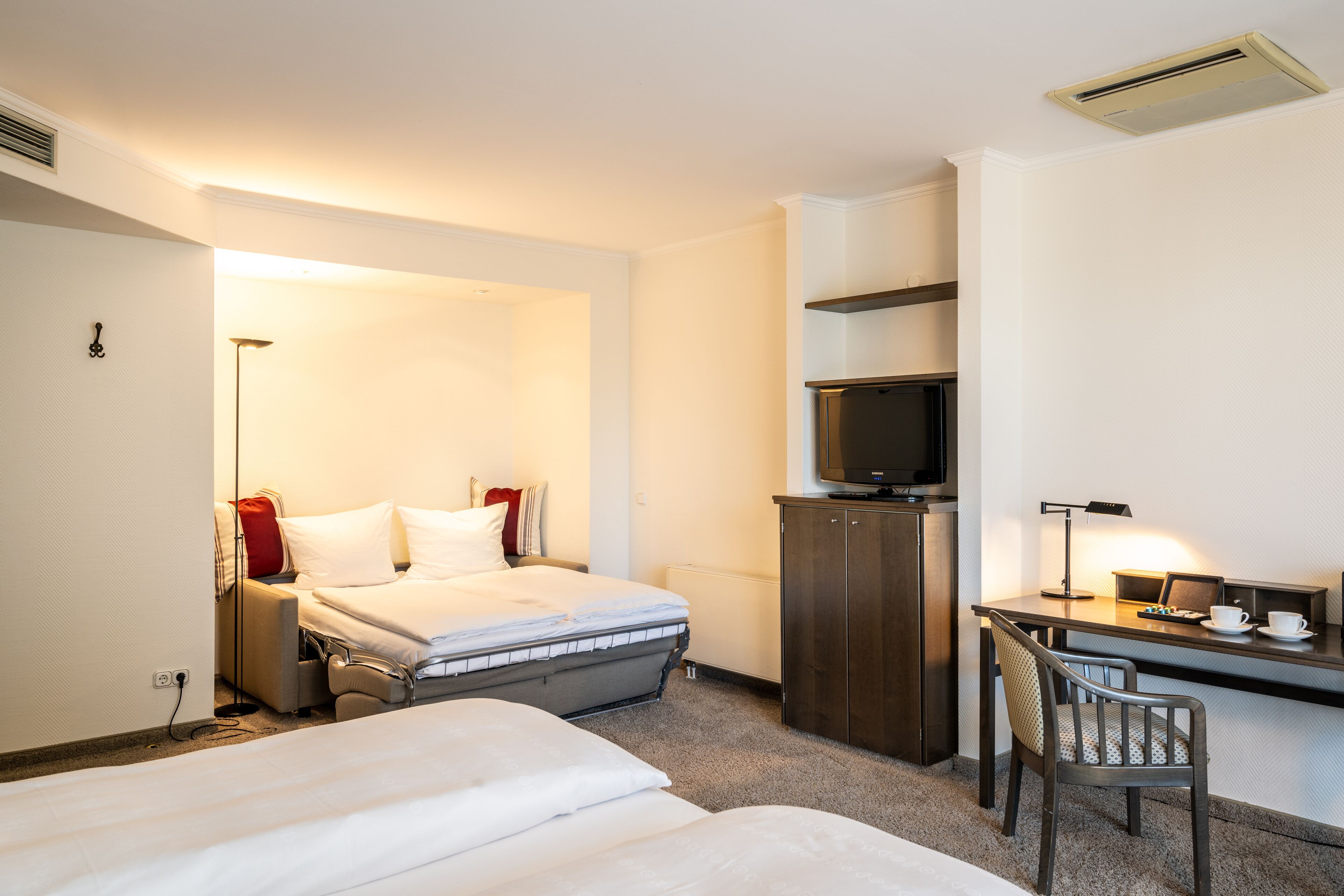 A hotel room with a bed, a desk with a chair, a television, and a lamp.