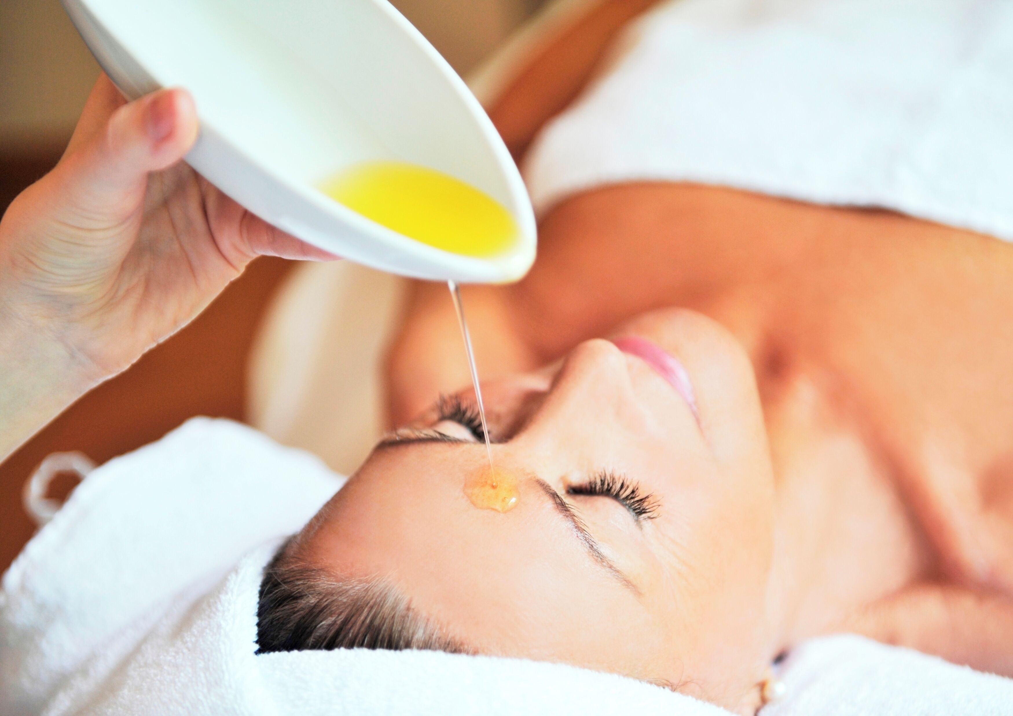 A person receiving a facial treatment with a bowl of yellow liquid being applied.