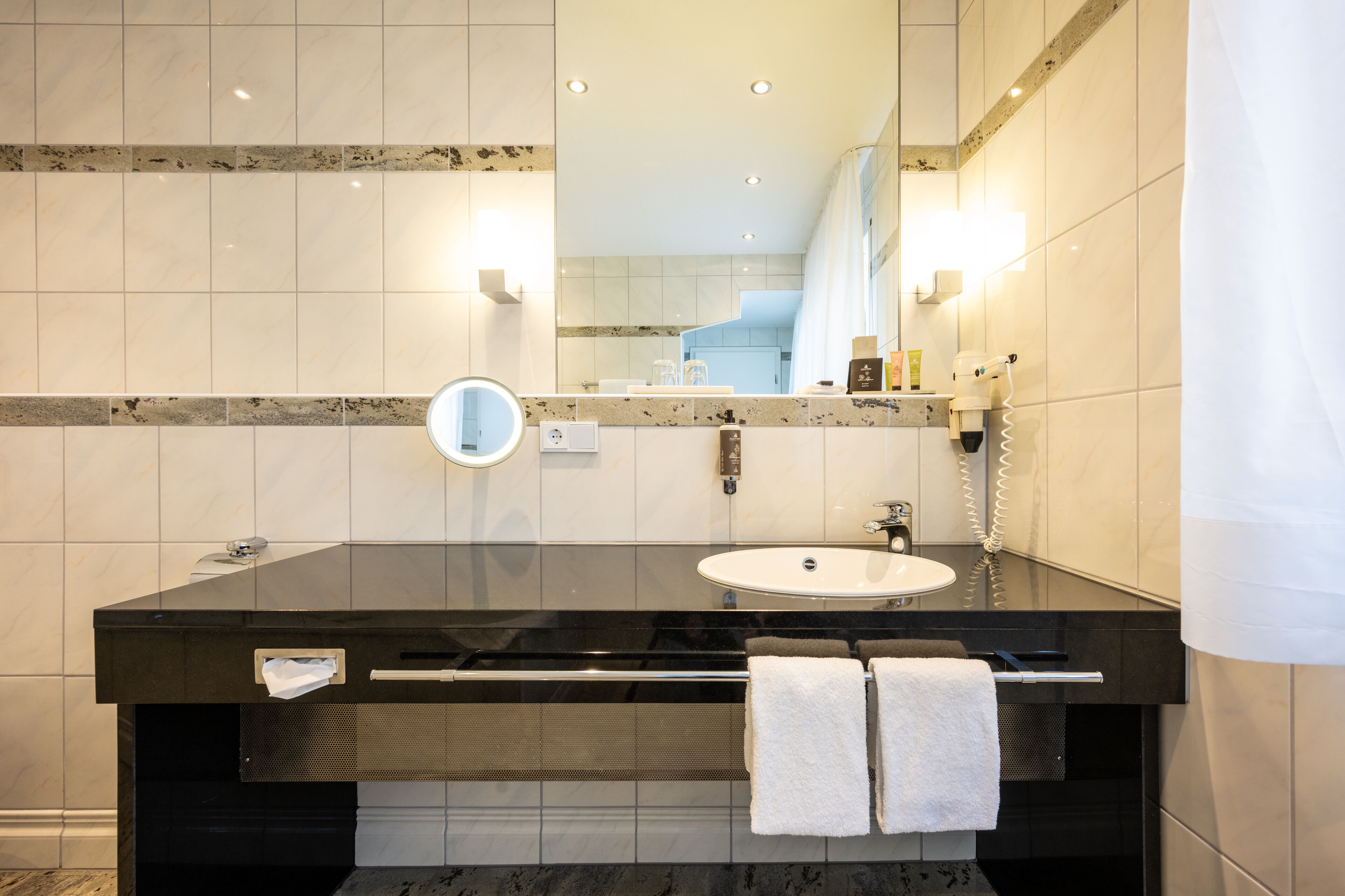 A modern bathroom with a black vanity, white sink, and a large mirror.