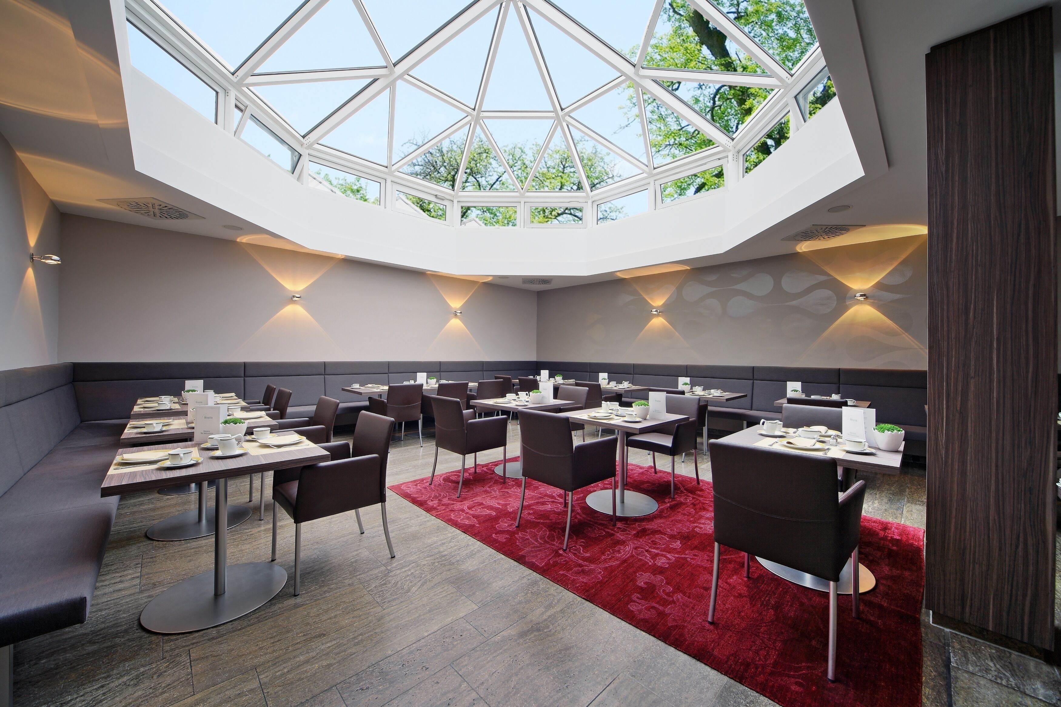 A modern dining area with a high ceiling and skylight, featuring tables and chairs arranged for dining.