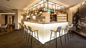 Zona de bar moderna con una isla central, taburetes y estantes llenos de botellas.