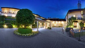 Un hotel con una entrada circular, un gran árbol en el centro y varios edificios con ventanas iluminadas.