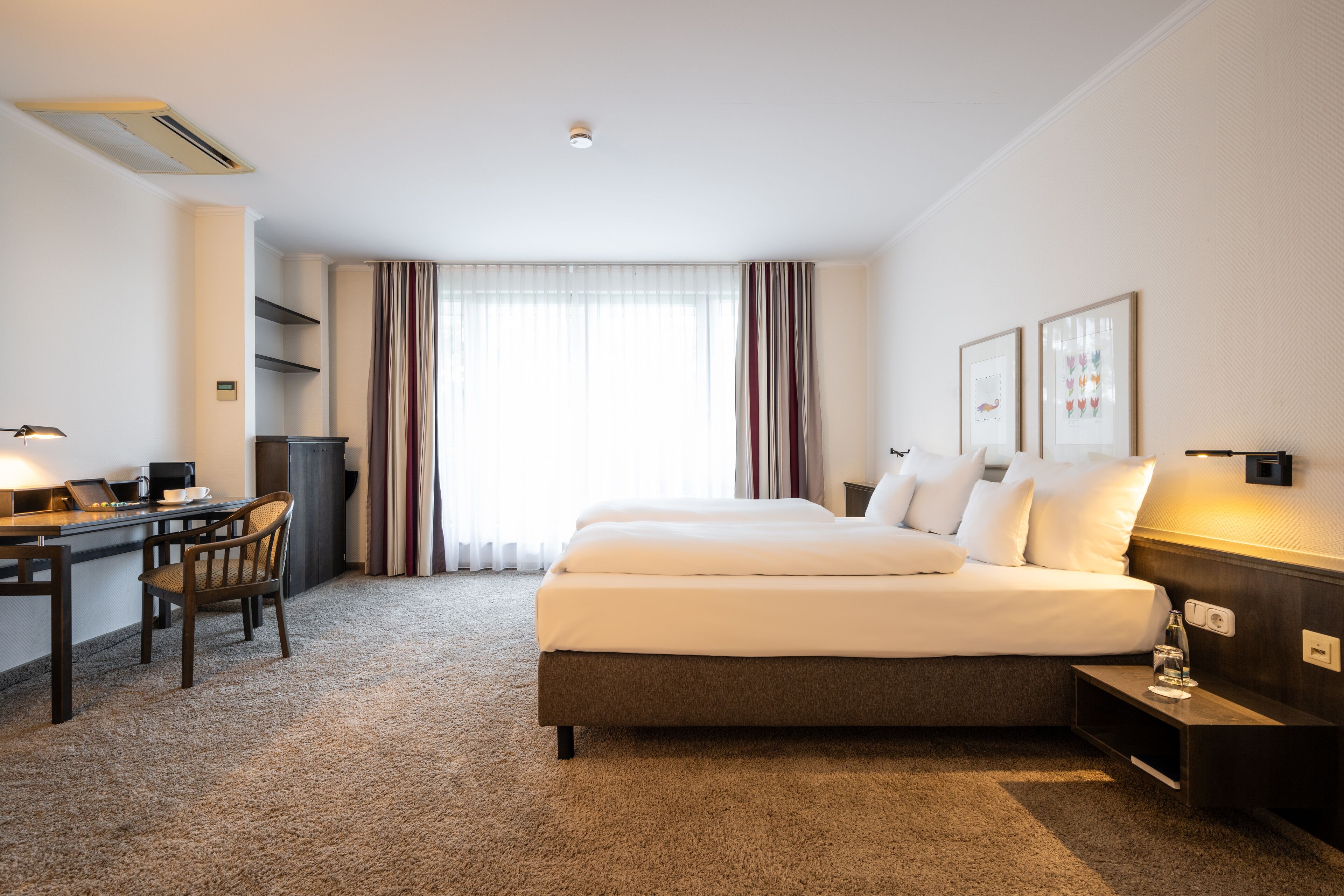 Ein Hotelzimmer mit einem großen Bett, einem Schreibtisch mit Stuhl, einem kleinen Tisch und einem Nachttisch.
