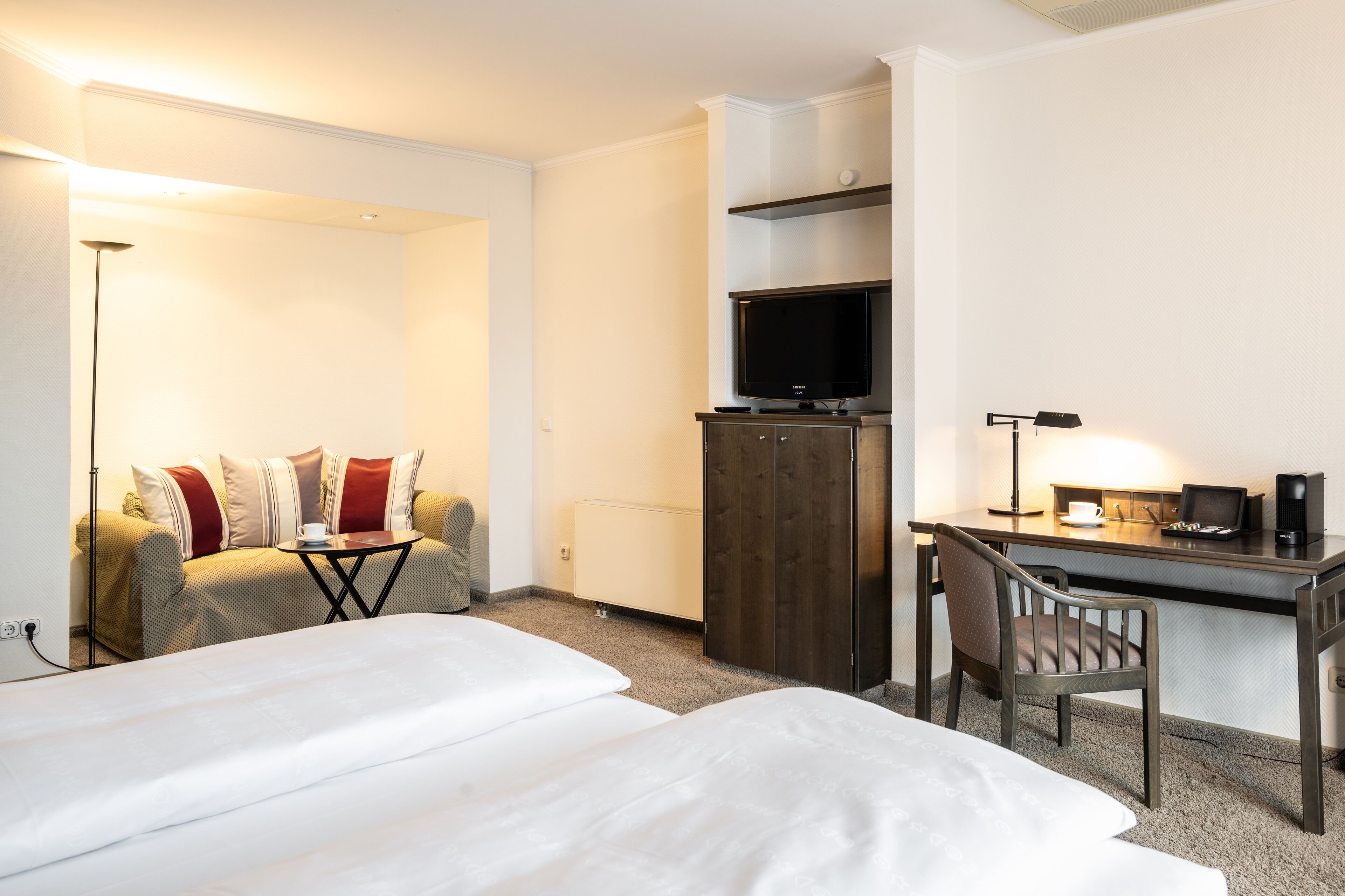 Een hotelkamer met twee bedden, een bureau met stoel, een televisie en een koffiezetapparaat.