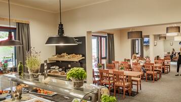 A restaurant with a buffet counter, wooden tables, and chairs.