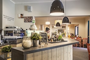 Una zona de bar con mostrador, máquinas de café y un menú en una pizarra.